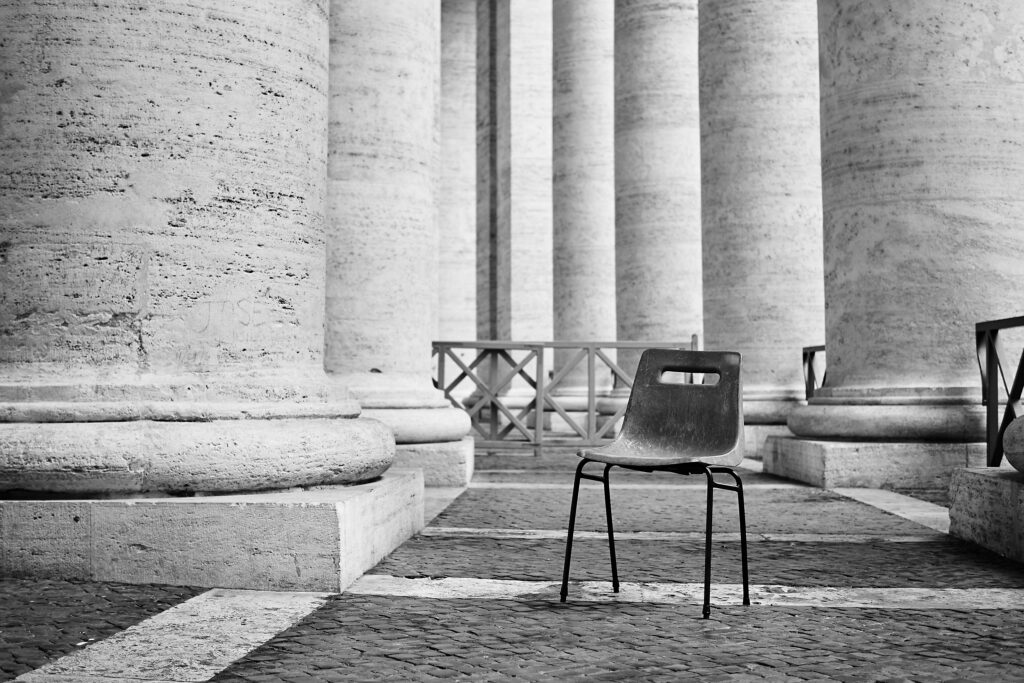 Grayscale shot of an abandoned plastic chair in a building with columns in Rome